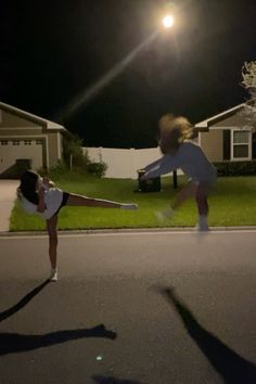 two people are doing tricks on the street at night with their hands in the air