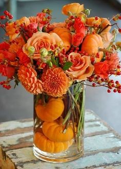 a vase filled with oranges and flowers on top of a table