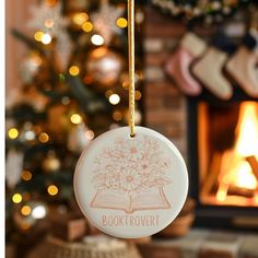 a book lover ornament hanging from a christmas tree in front of a fireplace