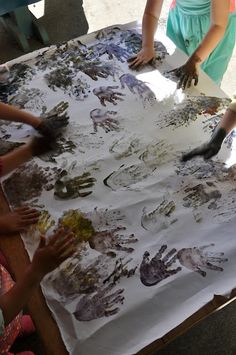 several children are sitting at a table with their hands on a large sheet of paper