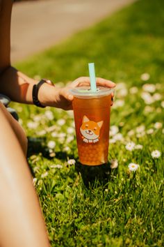 a person sitting in the grass holding a cup with a straw