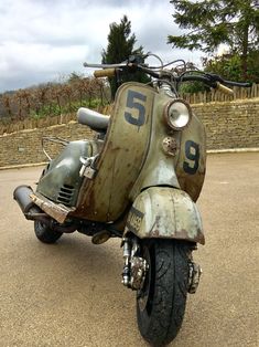 an old motorcycle parked in a parking lot next to a stone wall and tree line