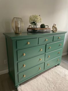 a green dresser sitting on top of a white rug next to a vase with flowers