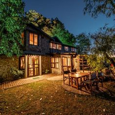 an outdoor dining table and chairs in front of a house at night with lights on