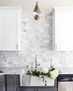 a white kitchen with marble backsplash and gold faucet light over the sink