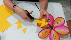 a person cutting paper with scissors on top of a white table covered in yellow and pink decorations