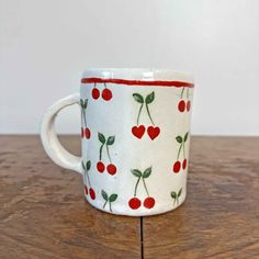 a white cup with cherries on it sitting on a wooden table