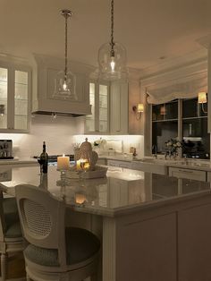 a kitchen with an island and bar stools next to the counter top, lights on