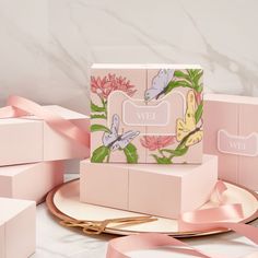 three pink boxes with flowers and butterflies on them, one has a ribbon tied around it