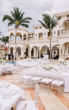 an outdoor wedding venue with tables and chairs set up in front of the building, surrounded by palm trees