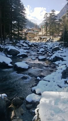 a river running through a forest filled with snow covered rocks and pine trees in the background