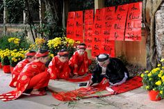 a group of people sitting on top of a red rug next to flowers and signs