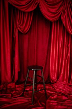 a stool sitting in front of a red curtain