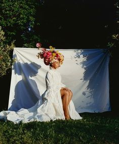 a woman with flowers in her hair sitting on the ground next to a white sheet