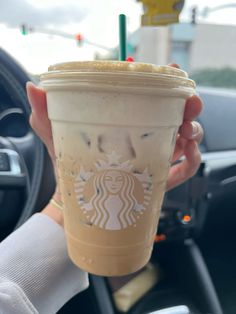 a person holding up a cup of coffee in their hand with the steering wheel behind them