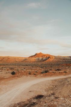 an empty dirt road in the middle of desert with mountains in the backgroud