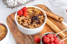 two bowls of food on a cutting board with raspberries and cinnamon sticks next to them