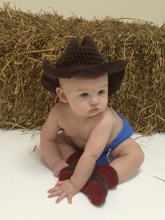 a baby wearing a cowboy hat and diaper sitting on the ground in front of hay bales