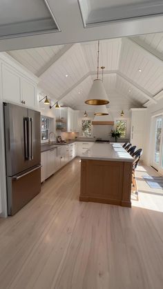 a large kitchen with white cabinets and wood flooring is pictured in this image, there are two pendant lights hanging from the ceiling