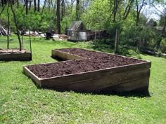 two wooden raised beds filled with dirt in the middle of a grassy area next to trees