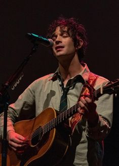 a man holding a guitar while standing in front of a microphone