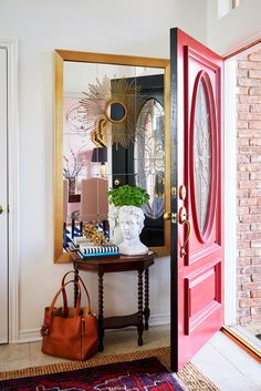 a red door is opened to reveal a mirror and purse on a table in front of it