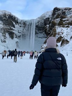 a group of people standing in the snow next to a waterfall with water falling from it