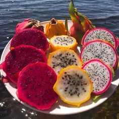 a plate full of different types of fruit on the water's edge, including dragonfruits