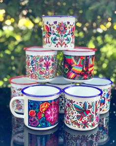 six colorful coffee mugs sitting on top of a black table with trees in the background