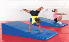 two girls doing tricks on trampoline mats in a gym