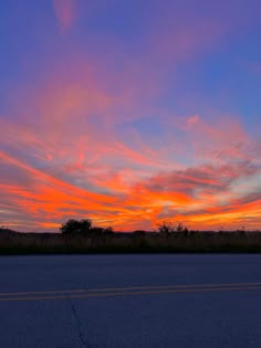 the sun is setting over an empty road with trees in the distance and blue sky