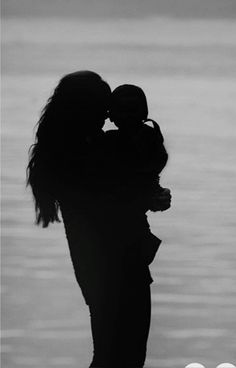 a couple kissing in front of the water with their hands on each other's shoulders