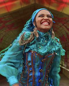 a woman wearing a blue and green outfit smiling at the camera with her hands in her pockets