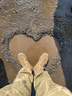 the legs and feet of a man in camouflage pants standing next to a heart shaped puddle