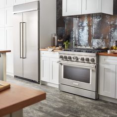 a stainless steel stove and refrigerator in a white kitchen with wood counter tops on the island