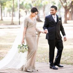 a bride and groom walking together in the park on their wedding day, holding hands