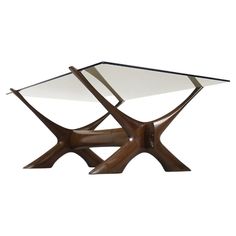 a glass and wood table with two intersecting sections on it's legs, in the shape