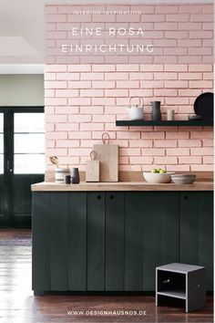 a pink brick wall in a kitchen with green cupboards and shelves on the side