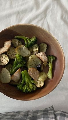 a brown bowl filled with broccoli and chicken on top of a white sheet