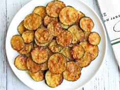 a white plate topped with fried zucchini on top of a table next to a napkin