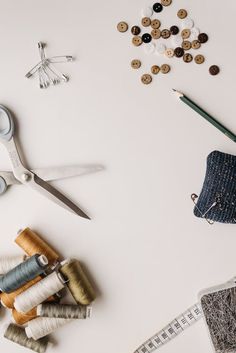 sewing supplies and scissors on a white surface with thread, needles, buttons and measuring tape