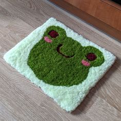 the rug is made to look like a green frog with eyes and nose, sitting on top of a wooden floor