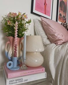 two vases with flowers are on top of books in front of a lamp and pictures