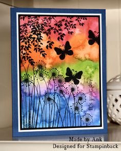 a card with butterflies and flowers on it, next to a white vase filled with watercolor