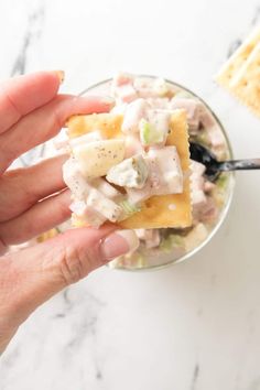 a hand holding a small bowl of food with crackers on the side and a spoon in it