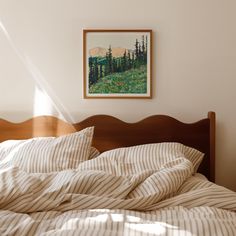 an unmade bed in a bedroom with a painting on the wall above it and sunlight streaming through the window