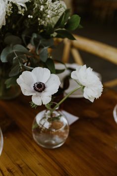 three white flowers in vases sitting on a wooden table with plates and napkins