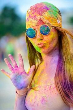 a young woman covered in colored powder making the peace sign with her hands and face