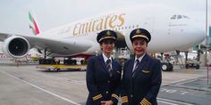 two pilots standing in front of an airplane on the tarmac with their arms around each other