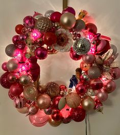 a christmas wreath is hanging on the wall with red and pink baubles around it